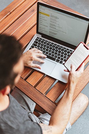 A man writing emails on his laptop whilst reading something on his phone