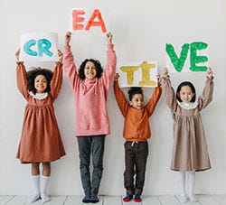 4 children holding up painted siugns which togethre read creative