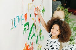 Girl smiling at camera whilst painging on a large canvas