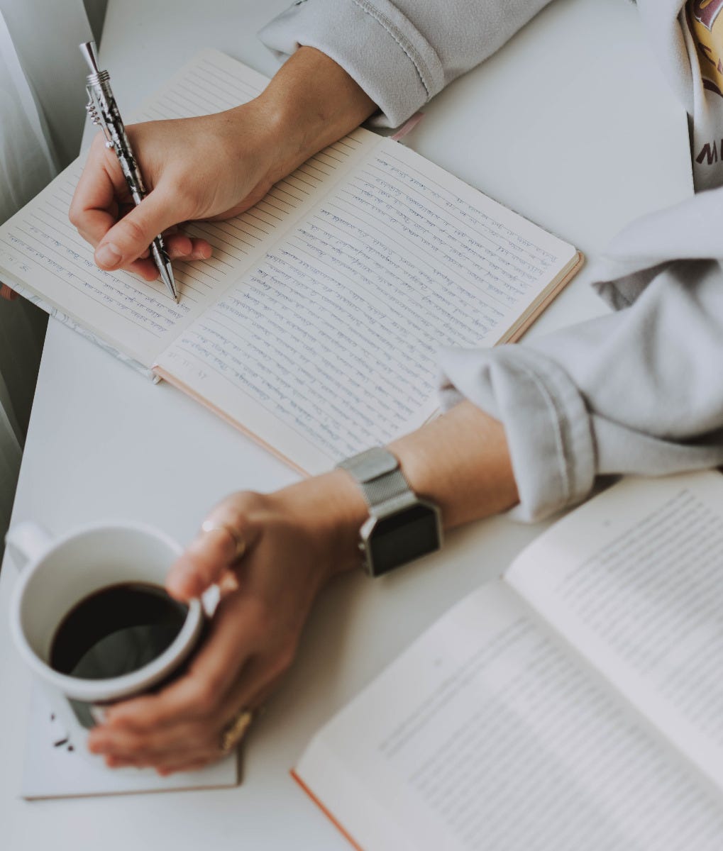 Person writing in a notebook while holding a coffee